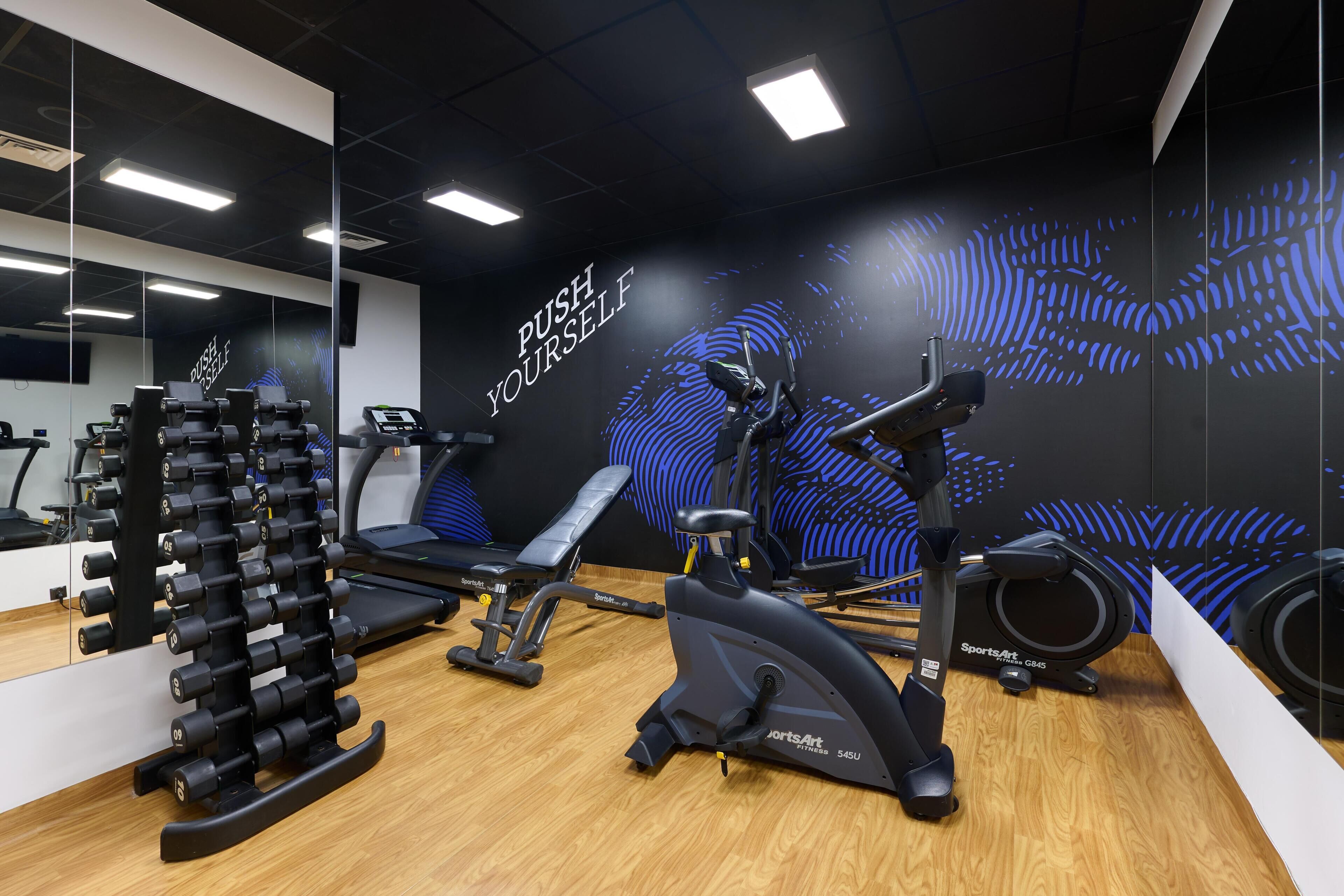 Un gimnasio con equipo de ejercicio, una banca y decoración inspiradora en las paredes.