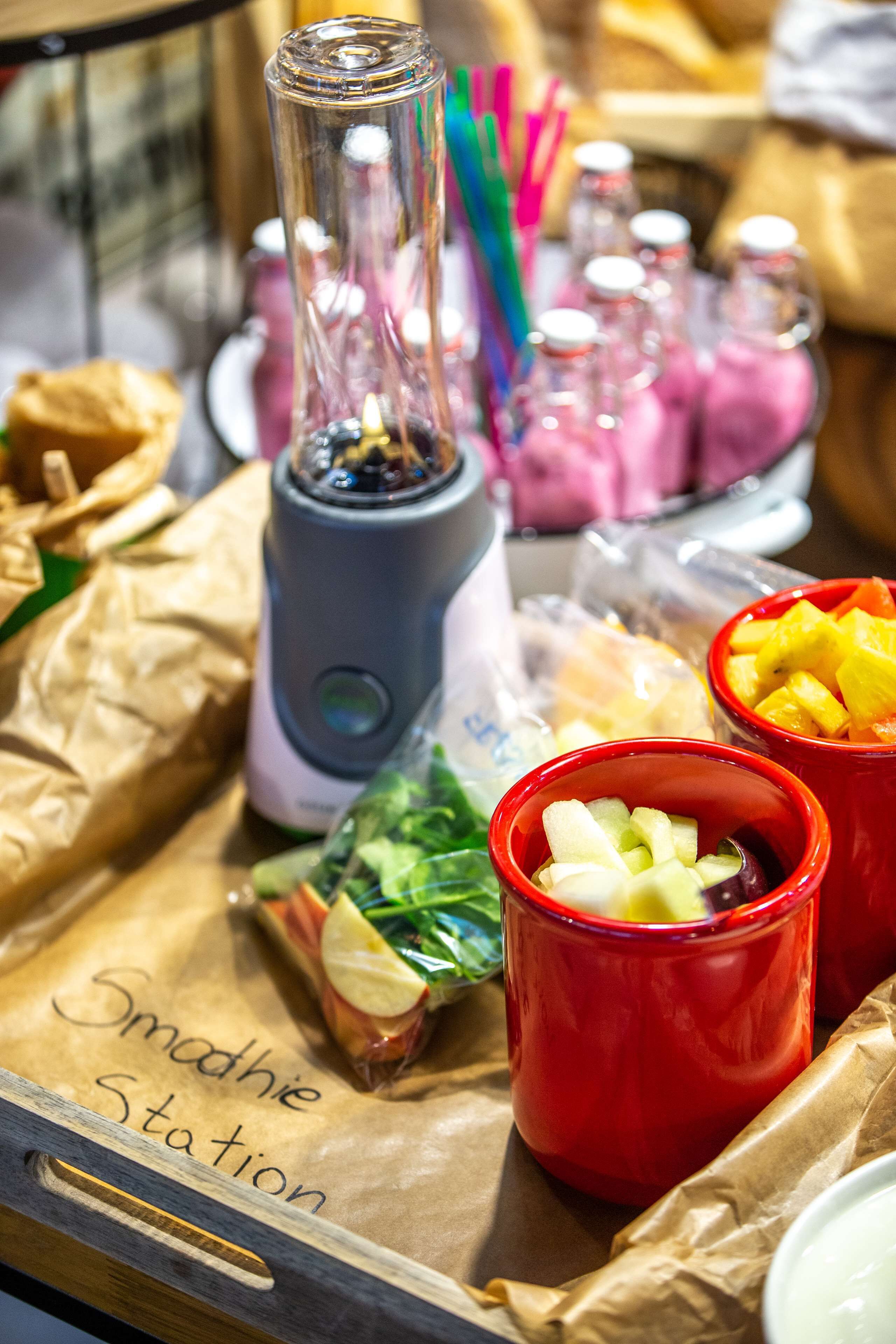 Un coin dédié aux smoothies, équipé d’un mixeur, de divers fruits et d’un sac en papier portant l’inscription « Coin à smoothies ».