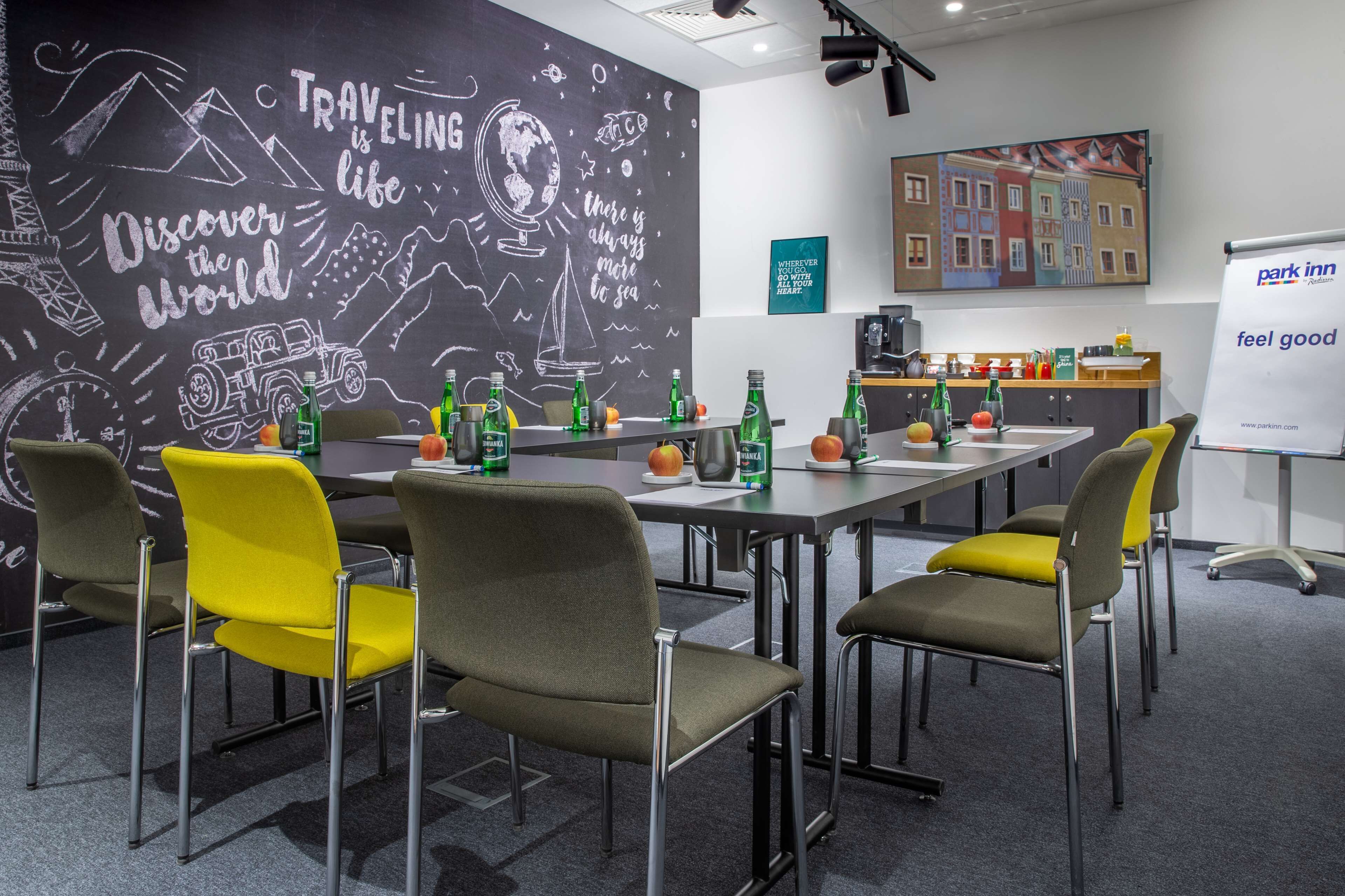 A conference room with a long table, multiple chairs, and a chalkboard wall with travel-themed drawings.