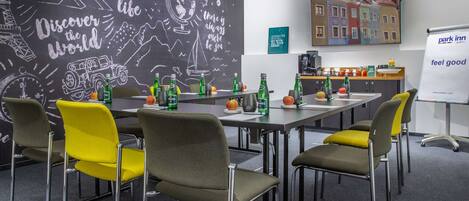 Un salón de conferencias con una larga mesa, varias sillas y una pared de pizarra con dibujos de temática viajera.