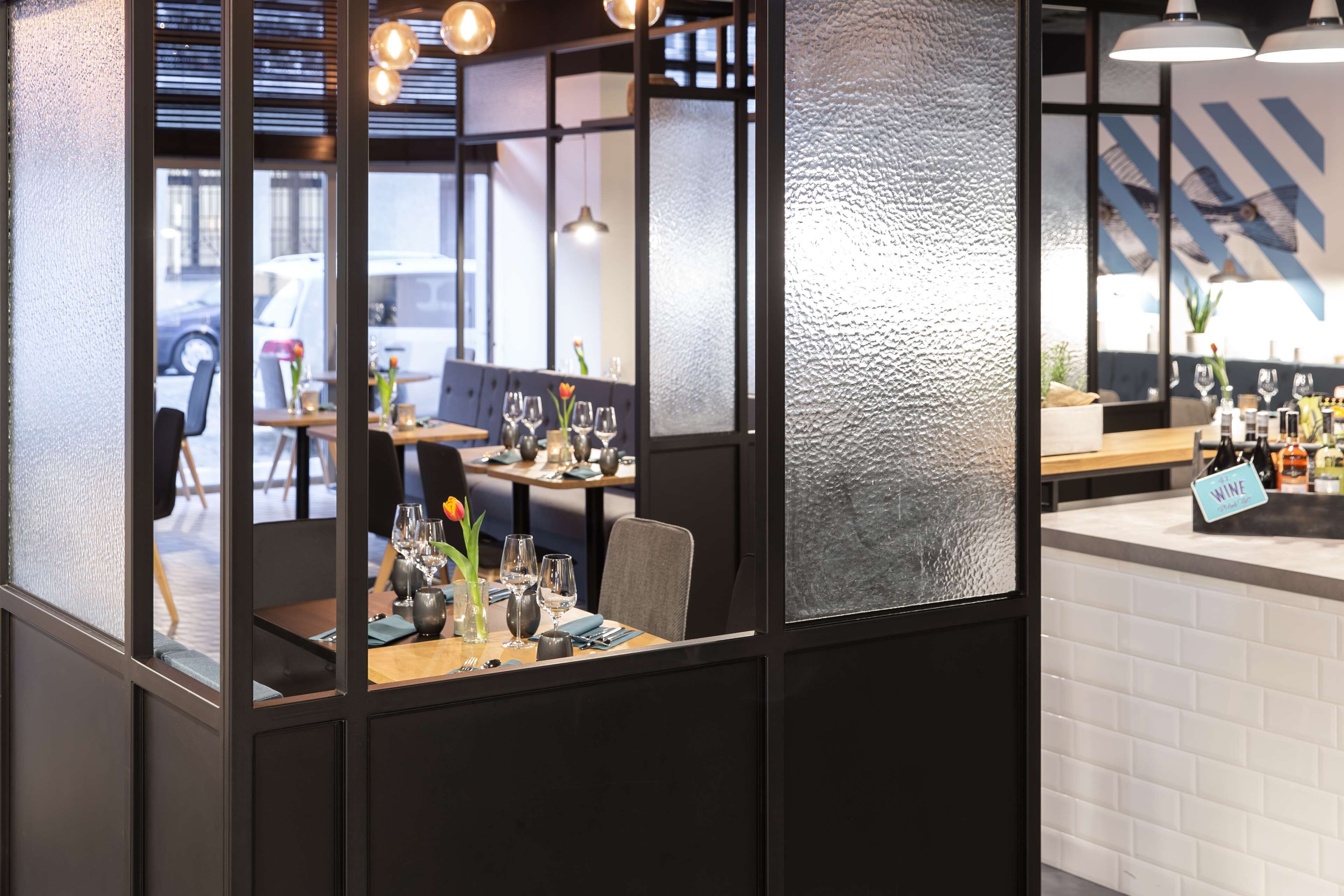 Un restaurant amb interior modern, decoració en blanc i negre, taules de fusta i una zona de bar de vi ben visible.