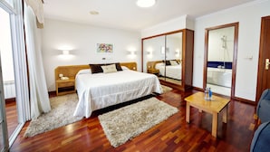 A hotel room with a bed, bedside tables, a wooden floor, a small table with bottles, and a mirror. - Hotel As Camelias (Arteixo)