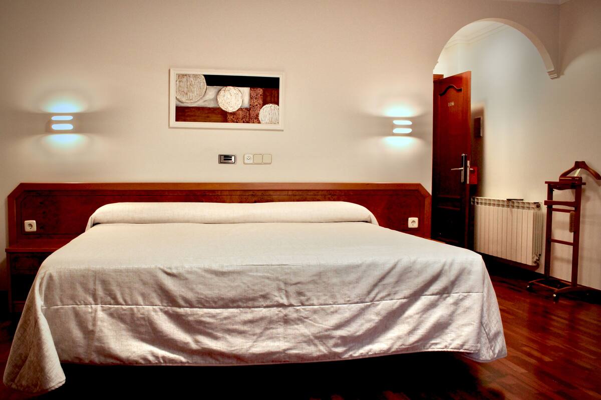 Quarto de hotel com uma cama grande, cabeceira de madeira, uma obra de arte na parede e um radiador.