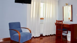 A room with a blue chair, a wooden desk, a mirror, and a television mounted on the wall. - Hotel As Camelias (Arteixo)