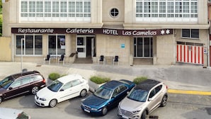 A hotel with a sign reading "HOTEL" and "Las Camelias" below. There are multiple cars parked in front, and the building has a tiled roof and multiple windows. - Hotel As Camelias (Arteixo)