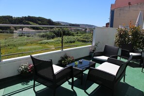 A balcony with wicker furniture, a table, and a view of a green landscape and distant buildings. - Hotel As Camelias (Arteixo)