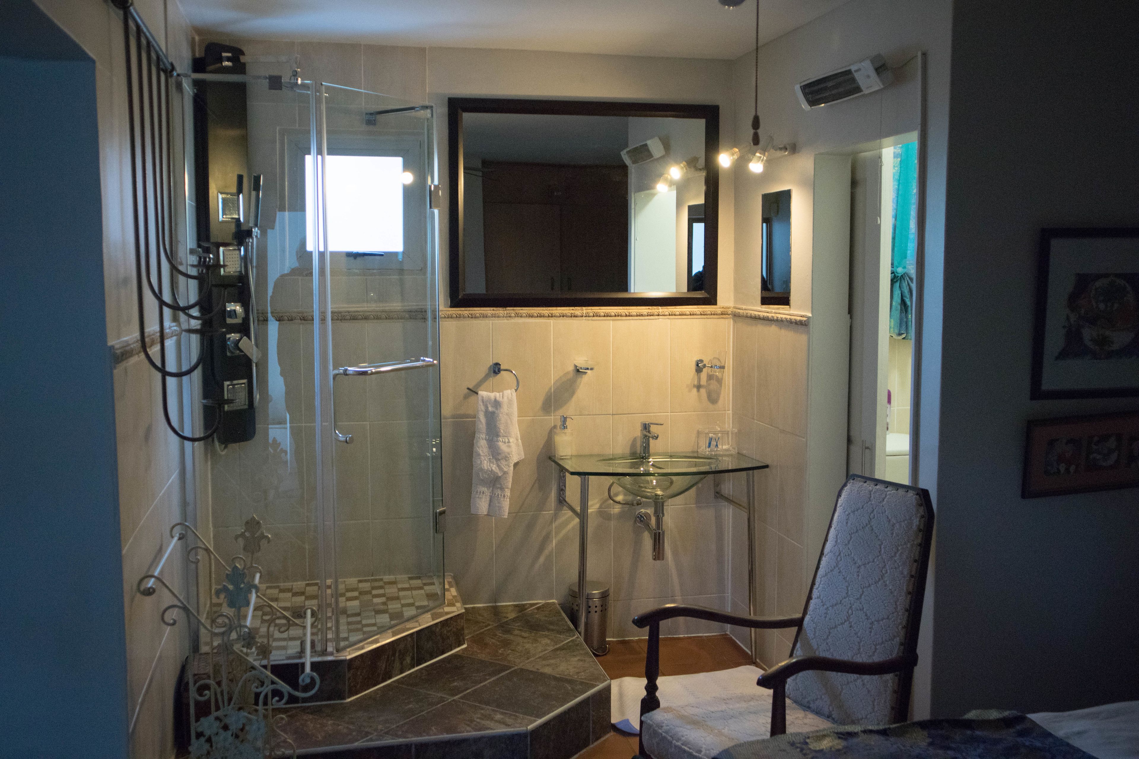 A bathroom with a glass shower enclosure, a sink, and a chair.