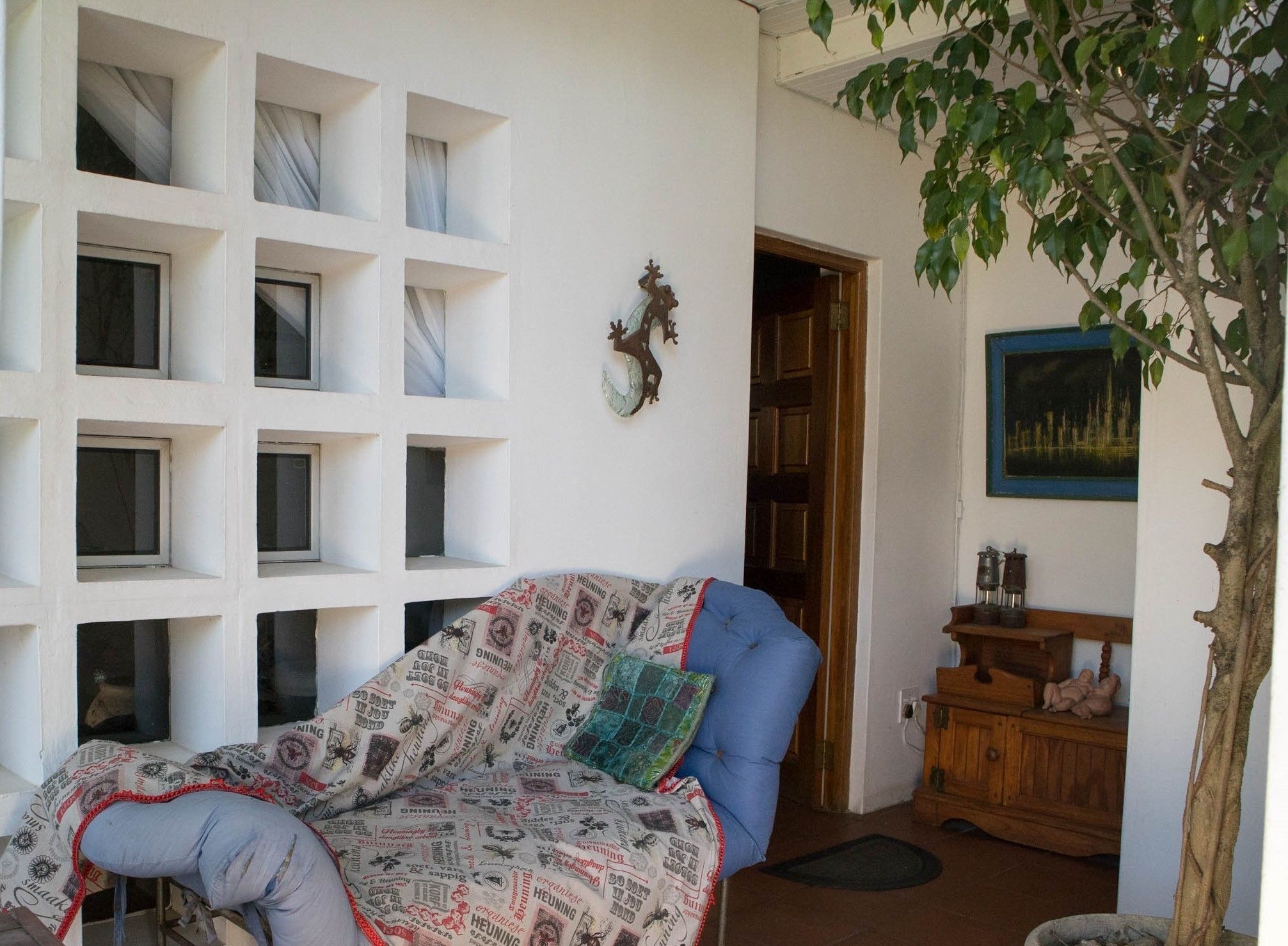 A room with a sofa covered in patterned fabric, a wooden cabinet with decorative items, a framed picture on the wall, and a tree in the corner.