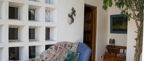 A room with a sofa covered in patterned fabric, a wooden cabinet with decorative items, a framed picture on the wall, and a tree in the corner.