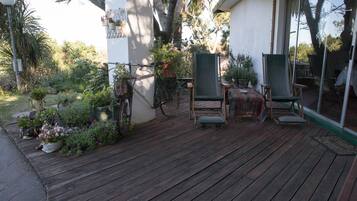 A wooden deck with outdoor furniture, surrounded by lush greenery and potted plants.