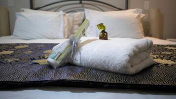 A neatly made bed with a folded white towel and a small gift box on a patterned bedspread.