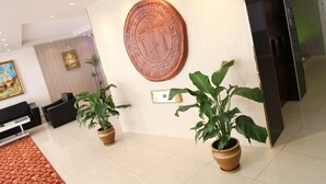 Un hall d’entrée orné d’une grande plaque en cuivre, de deux plantes en pot, d’un tableau et d’un comptoir de réception noir.