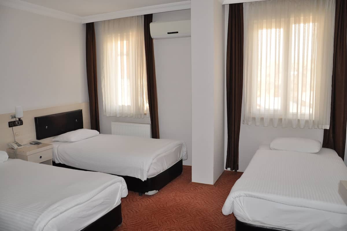 A hotel room with two single beds, a bedside table with a lamp, and a window with curtains.