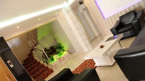 Un hall d’entrée avec un comptoir de réception, des canapés en cuir noir, un escalier agrémenté d’un mur d’accent vert et une moquette à motifs.
