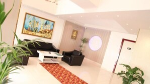 Un hall d’hôtel moderne avec un sol carrelé blanc, une moquette rouge à motifs, un canapé noir, une table basse blanche et un tableau accroché au mur.