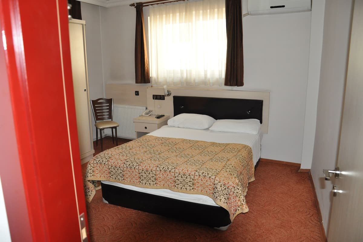 A hotel room with a bed, bedside table, chair, and a window with curtains.