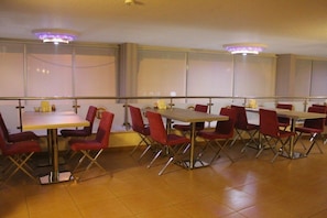 A dining area with multiple tables and red chairs, featuring a modern design with chrome legs and a clean, tiled floor.