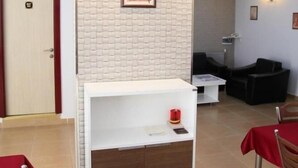 Un espace de vie moderne avec un meuble de rangement blanc pour les appareils multimédias, une cheminée et un coin repas agrémenté d’une nappe rouge.