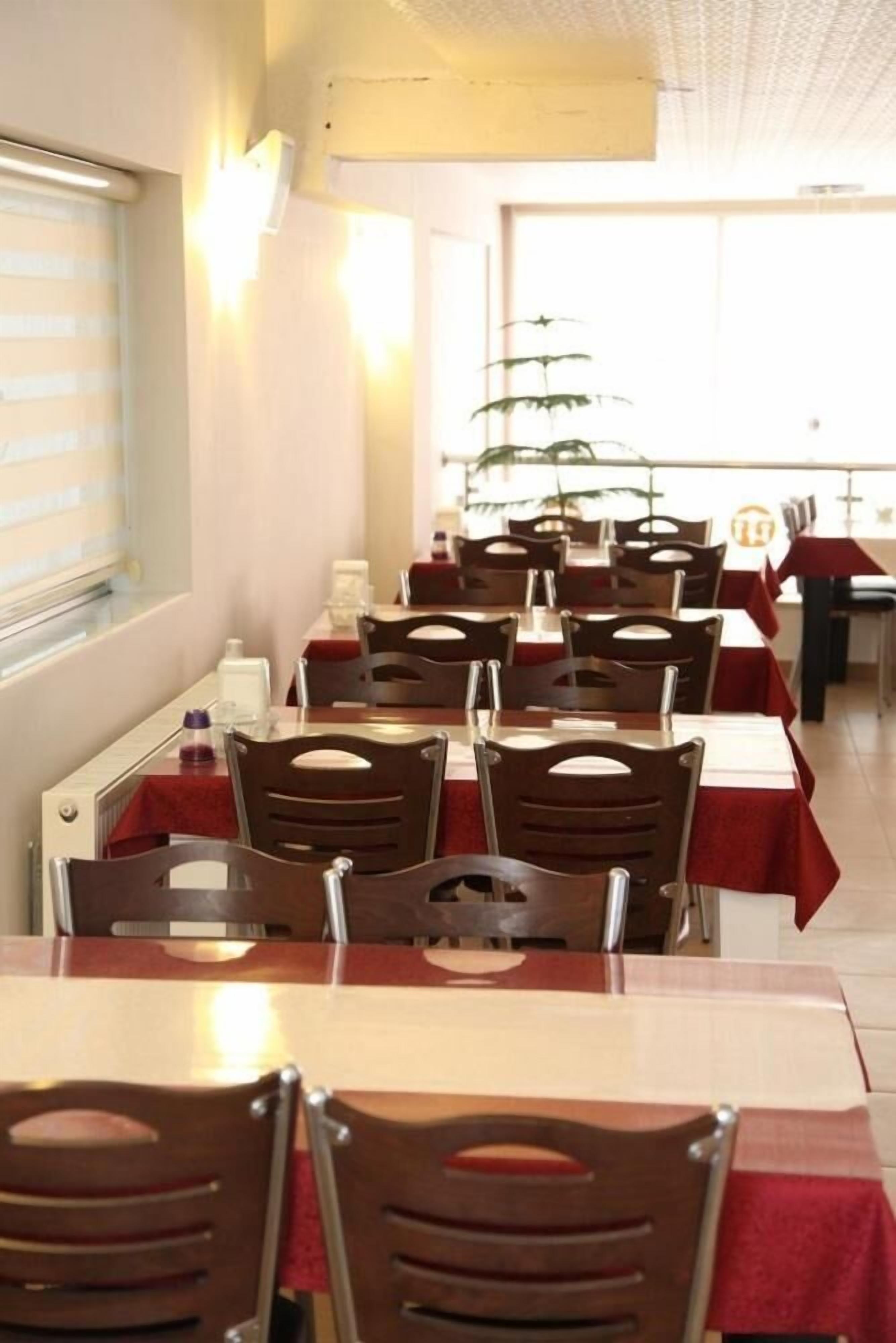 A restaurant with multiple tables and chairs, each covered with a red tablecloth.