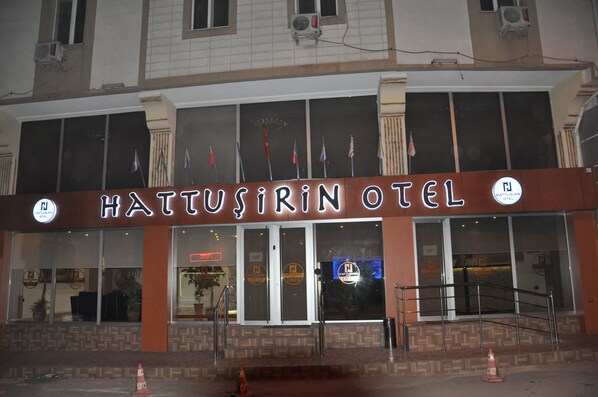 The exterior of Hattusirin Hotel with a prominent entrance, large windows, and multiple flags displayed outside.