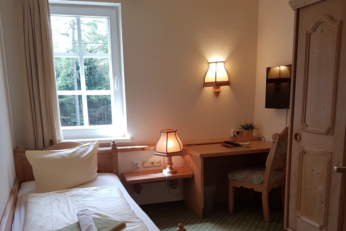 Un dormitorio con cama, escritorio, silla, lámpara, armario y ventana con cortinas.