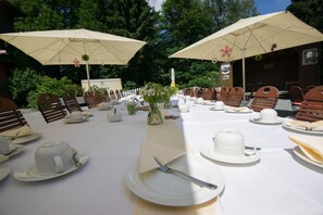 Une longue table à manger, dressée pour un événement formel en plein air, entourée de chaises et protégée par de grands parasols.