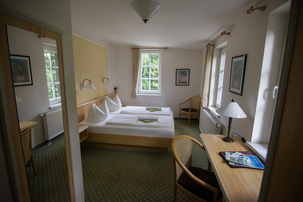 Habitación de hotel con dos camas, un escritorio, una silla, una lámpara y una ventana con cortinas.