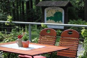 Un banc en bois avec une rambarde en métal, une table avec une carafe et une plante en pot, et un panneau en arrière-plan.