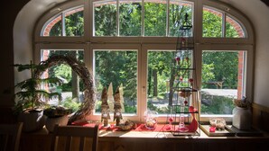 A room with a large arched window, a wooden table, and various decorative items including a wreath, small trees, and a birdcage.