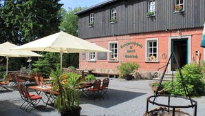 An outdoor seating area with tables and chairs, a fire pit, and a building with a sign that reads "Bergwiesen & Biergarten".