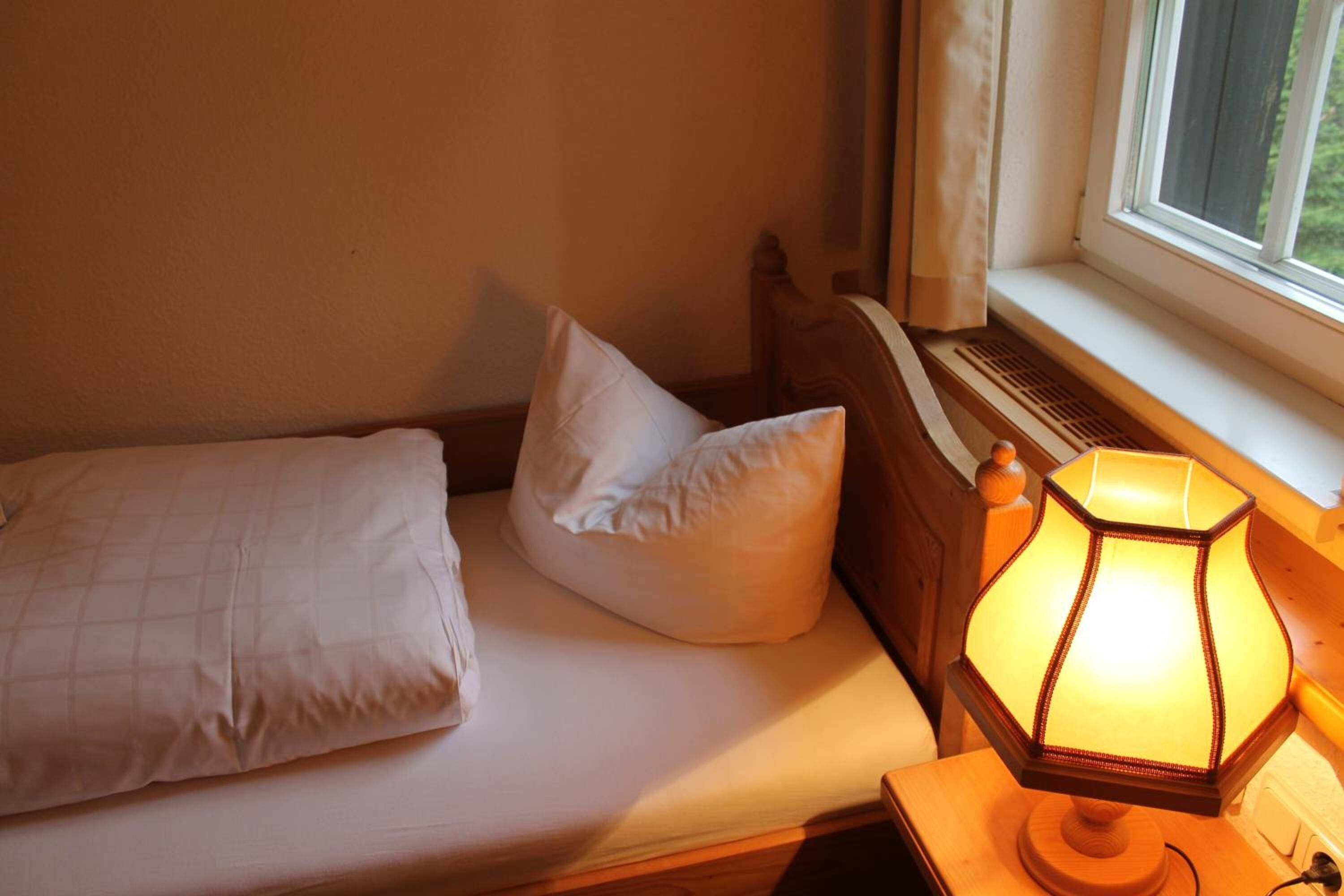 A bed with white bedding, a lamp on a bedside table, and a window with curtains.