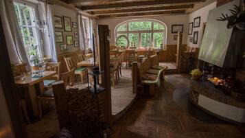 A cozy, rustic dining area with wooden furniture, a fireplace, and a large arched window providing natural light.