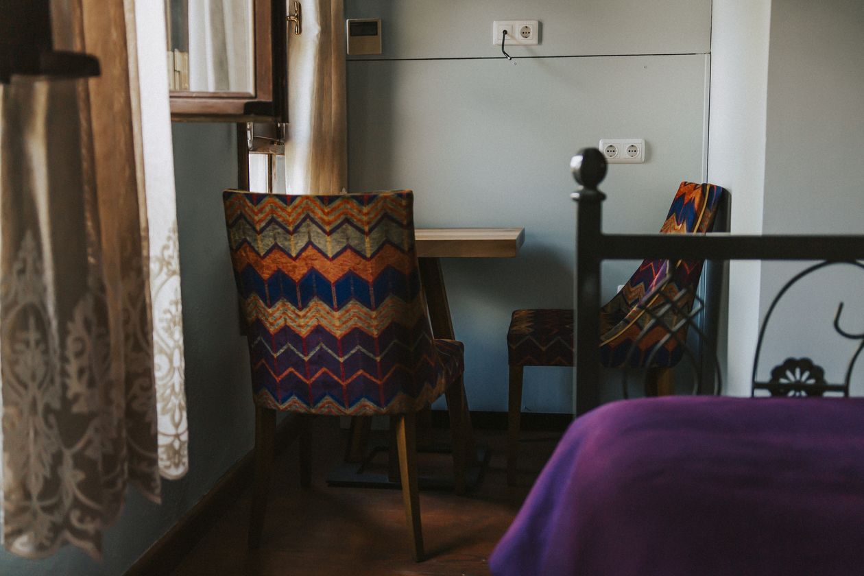 Una habitación con cama, una silla, una mesita y un enchufe.