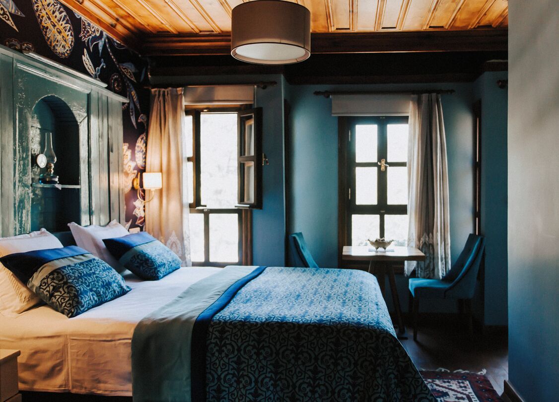 Una habitación con una cama grande, dos ventanas, una mesa y una silla.