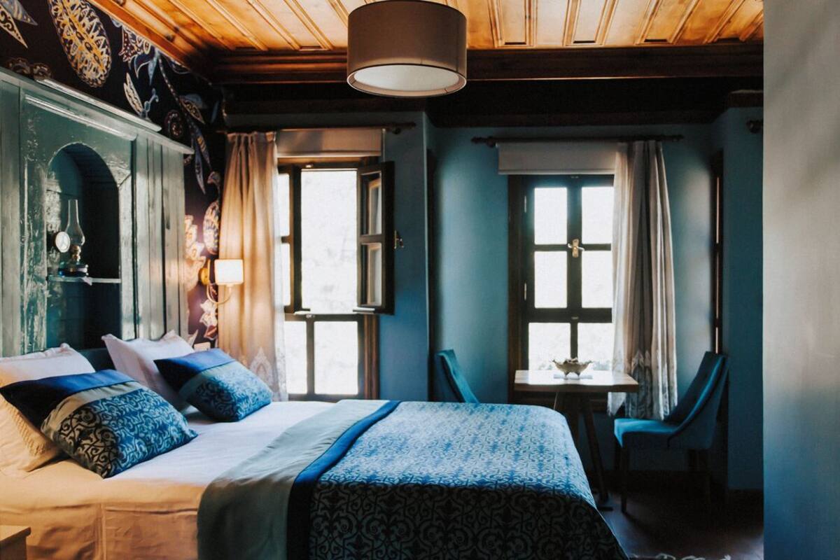 Una habitación con una cama grande, dos ventanas, una mesa y una silla.