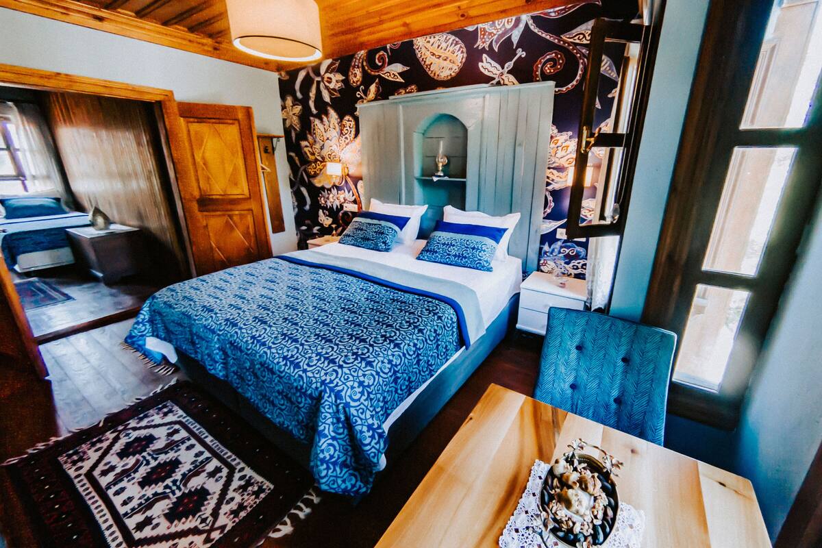 Un dormitorio con una cama, una mesita de noche, una silla, una mesa y una ventana.