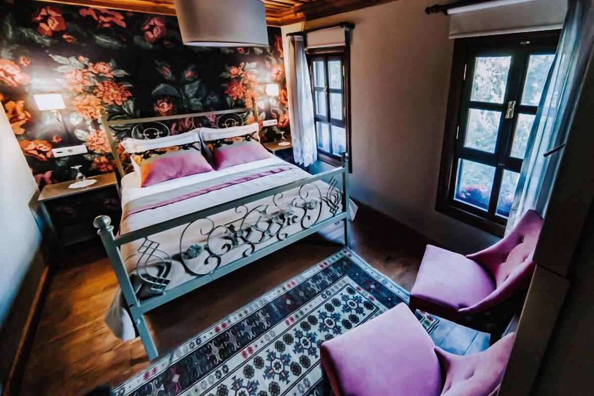 A bedroom with a bed, a nightstand, a chair, a window, and a floral wallpaper.