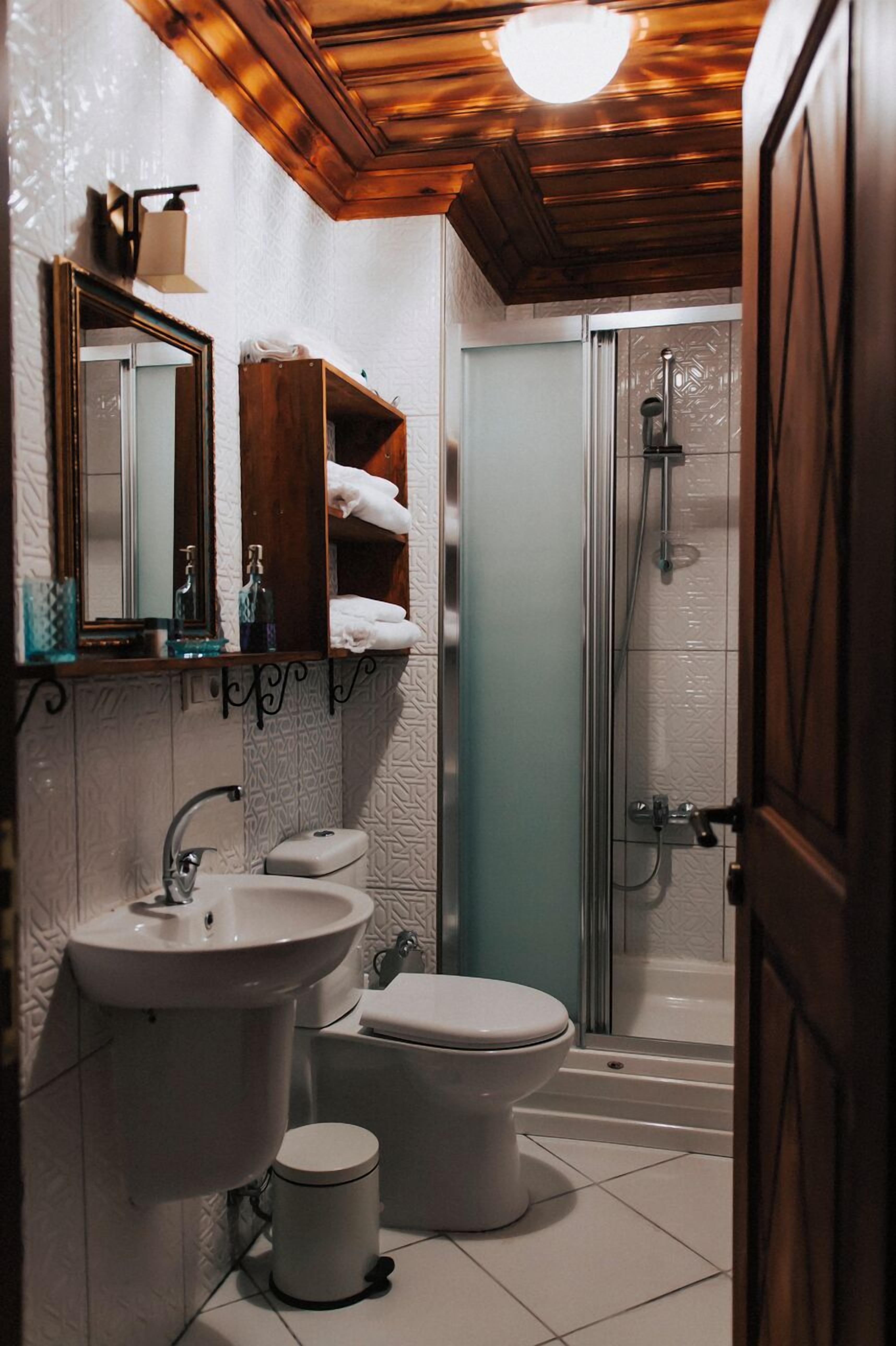 Un baño con techo de madera, un lavabo, inodoro, ducha y espejo.