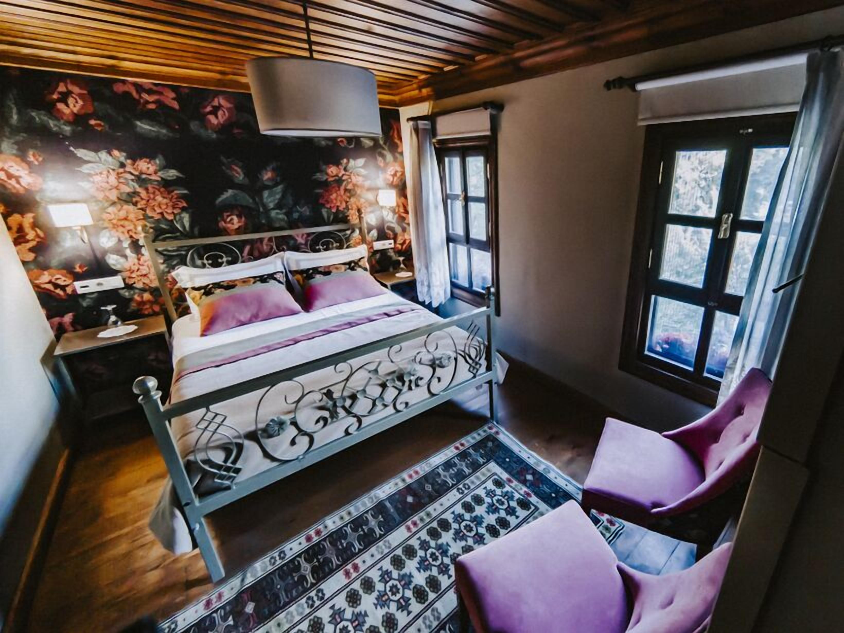 Quarto com cama, mesa de cabeceira, cadeira, janela e papel de parede floral.