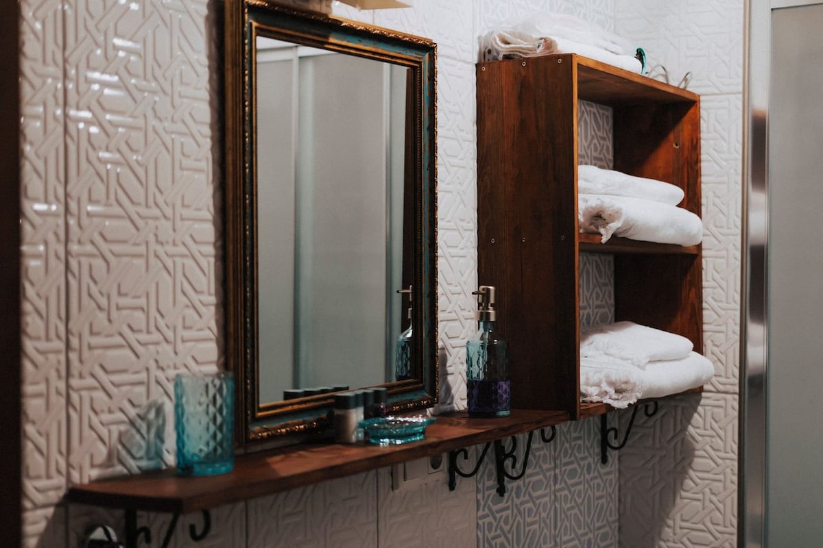 A bathroom with a mirror, a shelf with towels, and a patterned wall.