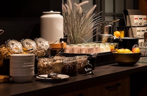A buffet setup with various food items, including jars of pickles and a large white container, likely for beverages.