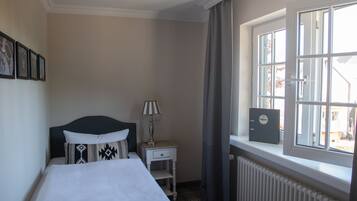 A hotel room with a bed, a nightstand, a lamp, a window with curtains, and a radiator.