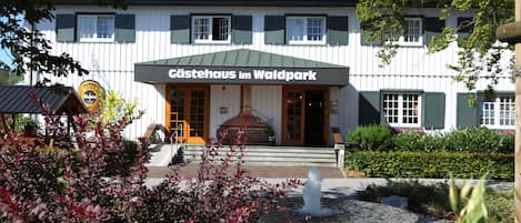 Ein Gebäude mit einem Schild, auf dem "Gästehaus im Waldpark" steht, und einem Brunnen im Vordergrund.