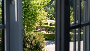 Blick durch ein Fenster auf einen Gartenbereich mit Sitzgelegenheiten im Freien und einem Weg.
