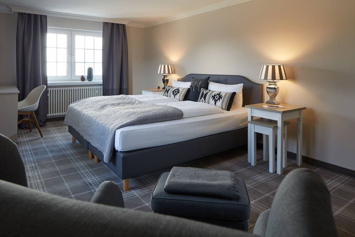 A hotel room with a large bed, two bedside tables with lamps, a chair, and a view of the outdoors through a window.