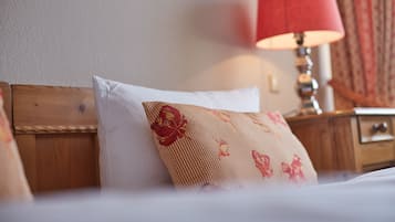 Siististi pedattu sänky, jossa on puinen pääty, punainen lamppu yöpöydällä ja kukkakuviollinen tyyny.
