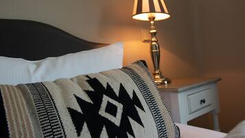 A bed with a patterned pillow, a bedside lamp, and a small white nightstand with a drawer.