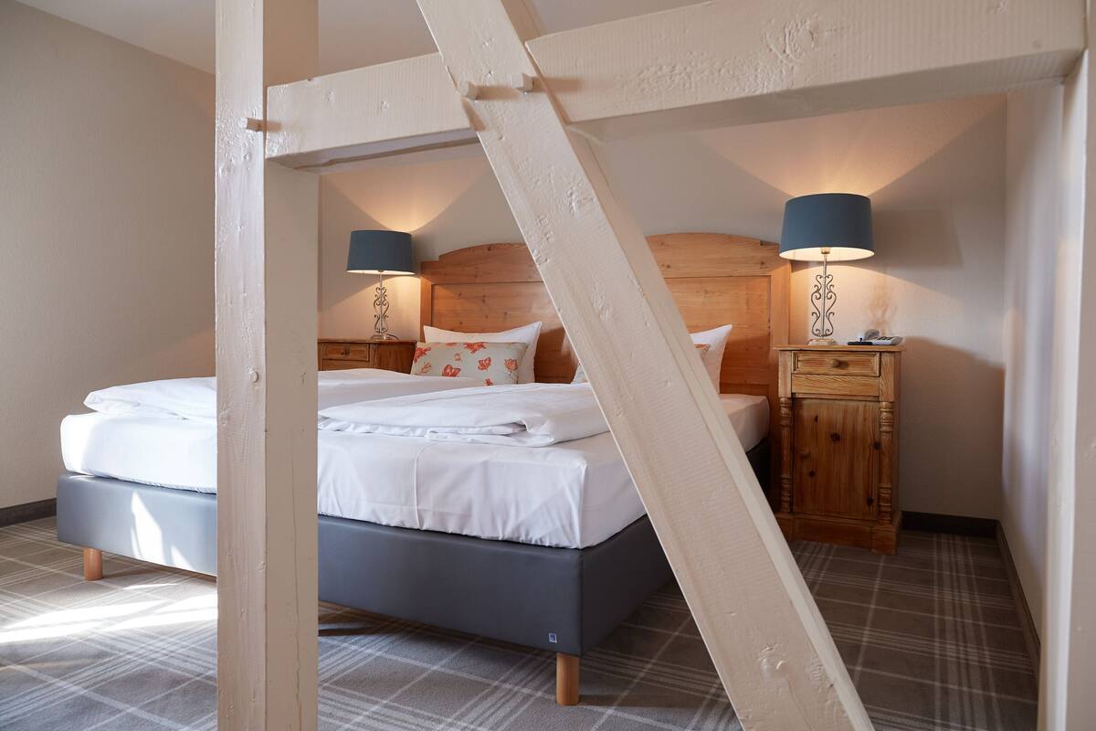 A bedroom with a bed, wooden headboard, two bedside tables with lamps, and a plaid floor.