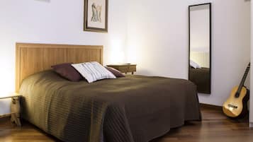Una camera da letto ordinata con una testiera in legno, un letto con cuscino a righe, un comodino con una lampada, una chitarra e uno specchio grande.