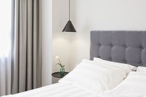A neatly made bed with white linens, a grey upholstered headboard, and a small bedside table with a vase of flowers. - The Artist Athens (Athens)
